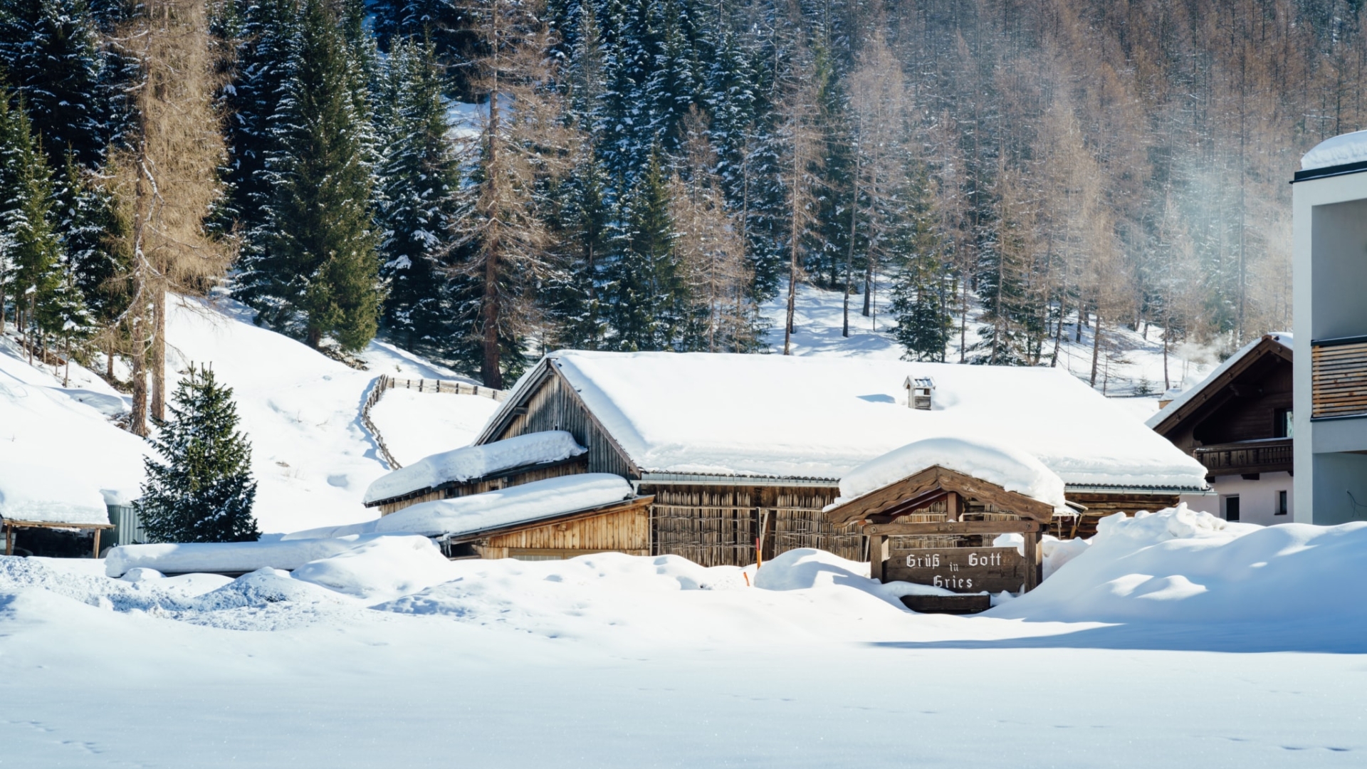 Traditionelles Holzhaus im Winter mit verschneiter Landschaft und Kiefern im Hintergrund