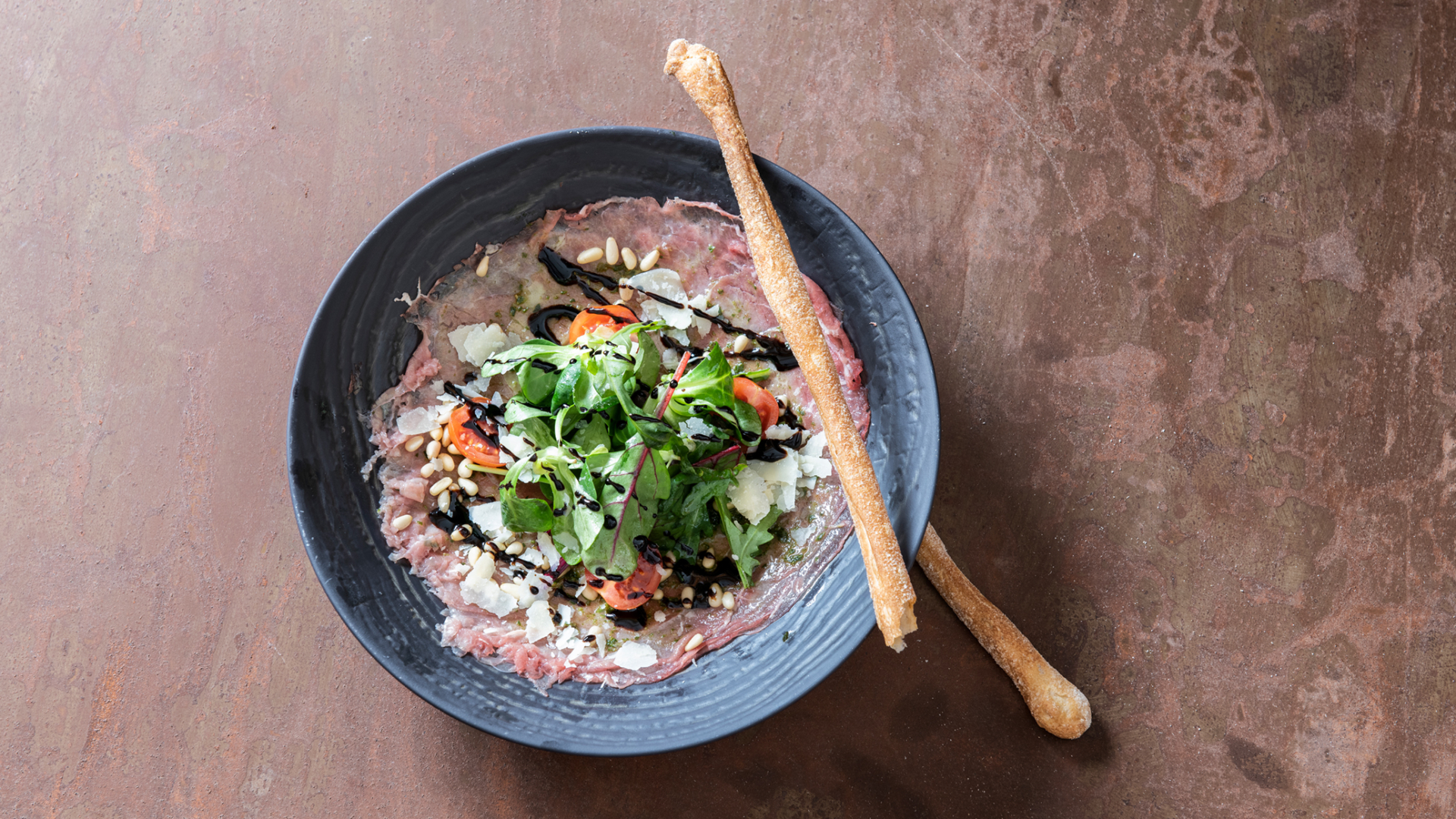 Leckeres Carpaccio in schwarzem Teller mit frischem Salat und gerösteten Pinienkernen