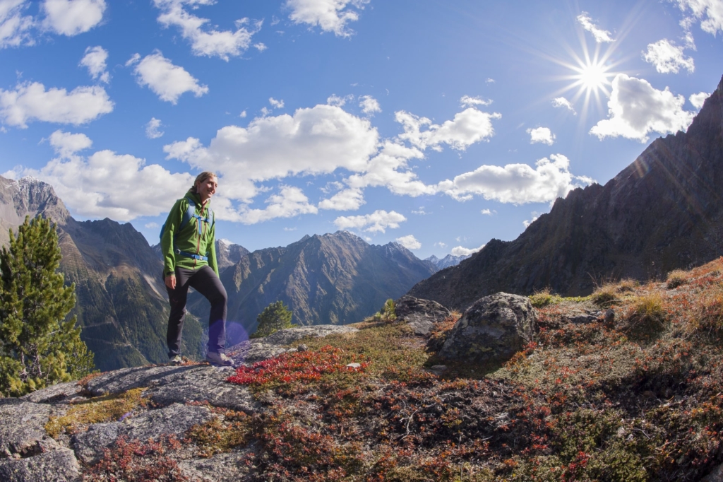 Wanderer auf einem Felsen in den Alpen mit Blick auf die Berge und blauen Himmel